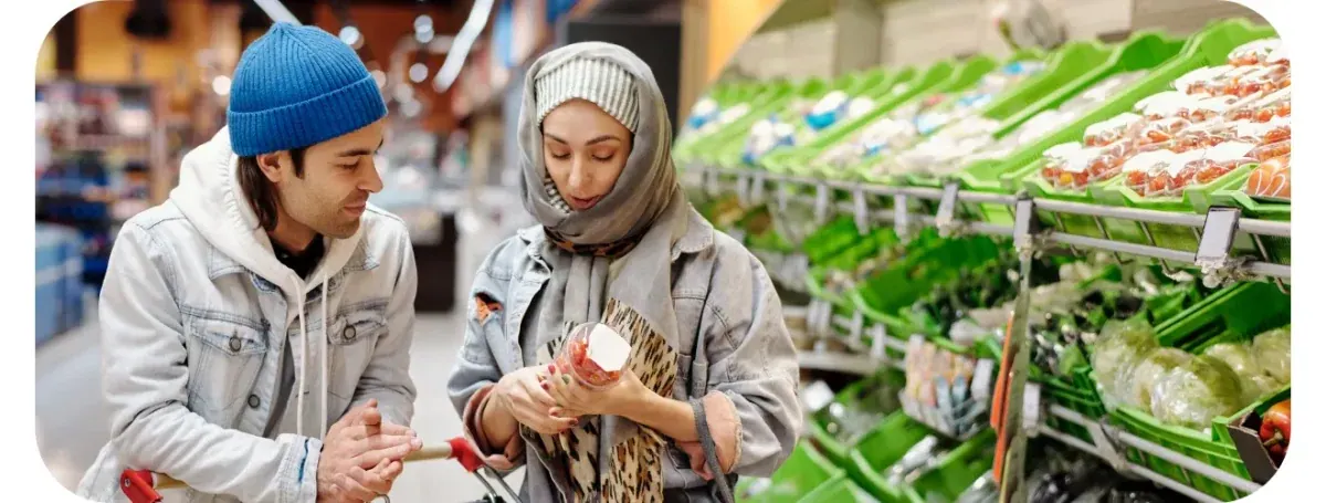 A couple with a shopping trolley reading the label on a punnet of strawberries, beside a long run of green crates of fruit and vegetables.