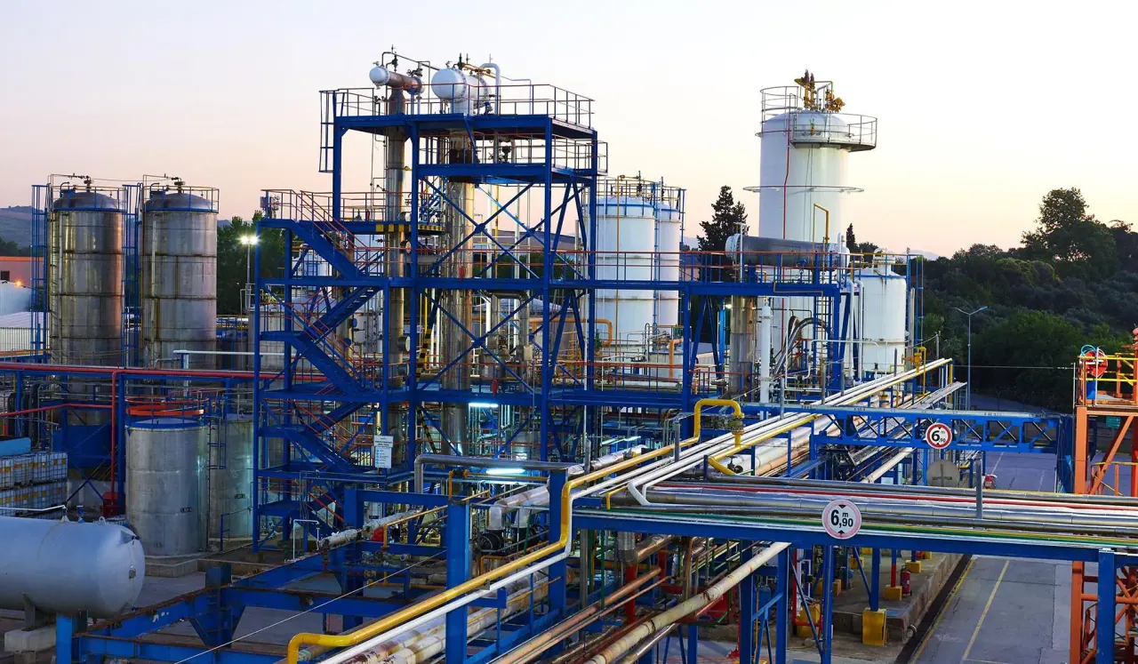 A chemicals plant at dusk, tanks and pipework lit against the sky