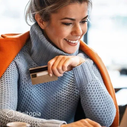 A smiling woman in a café holding a payment card in front of her laptop