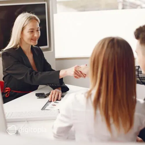 A bank adviser shaking hands with two customers across her desk