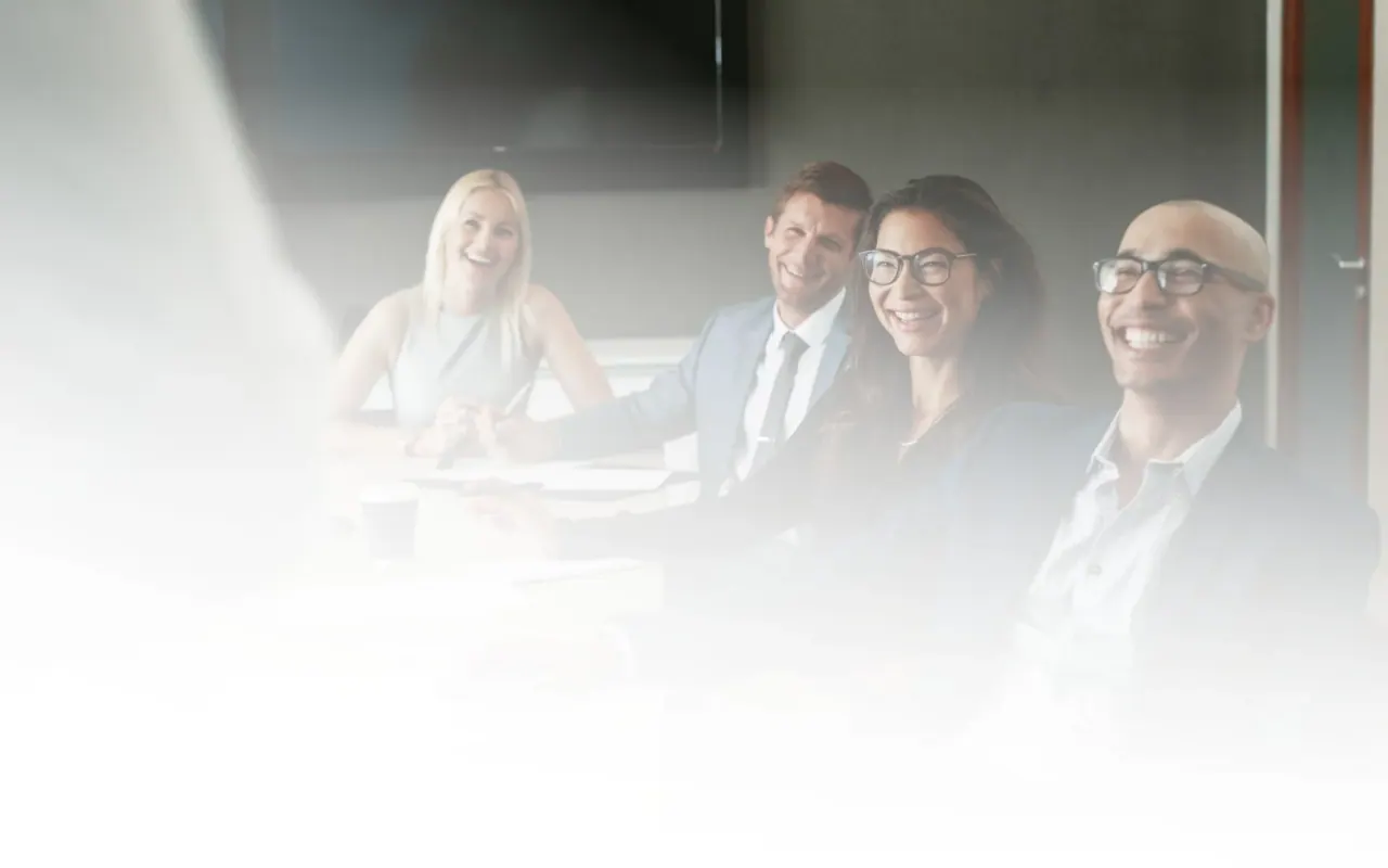 Four colleagues laughing around a boardroom table during a meeting