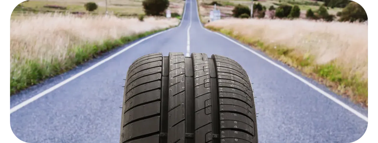 A tyre seen tread-on in the middle of an empty country road running straight to the horizon between fields of dry grass.