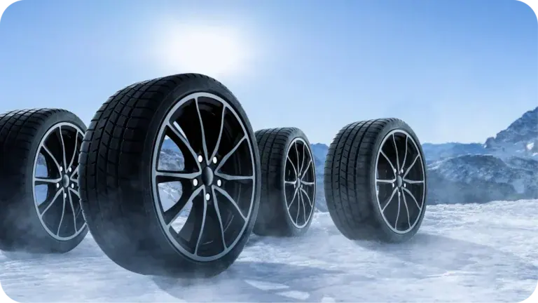 Four Bridgestone winter tyres on alloy wheels standing on a snowfield under a bright low sun, mountains behind them.