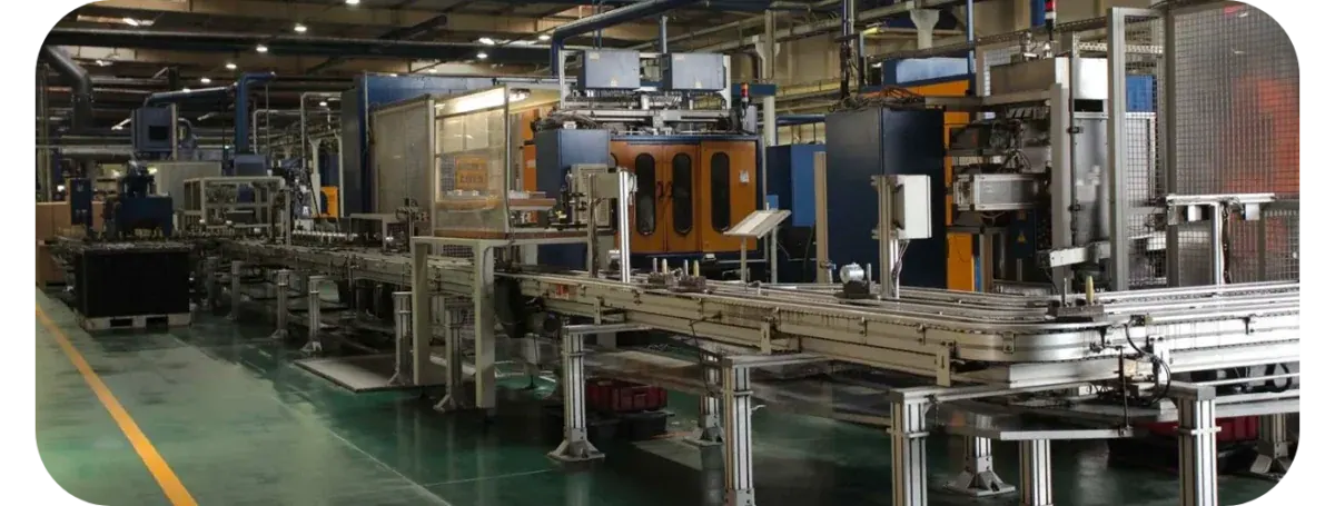 A conveyor running the length of a Federal Mogul production hall, past blue and orange machining cells and safety cages, on a green-painted floor.
