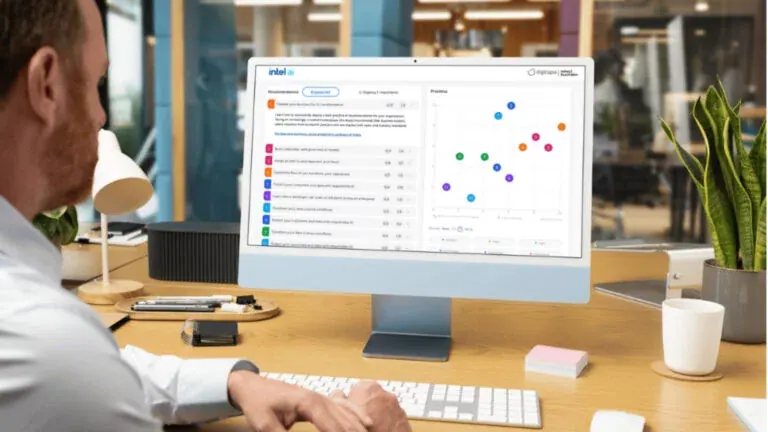 A man at a desk reading his AI Readiness Assessment results, a list of recommendations beside a priorities chart, on an iMac, in a daylit open office.