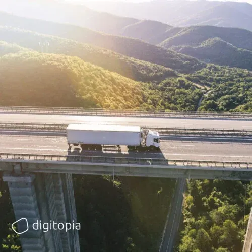 A white articulated lorry crossing a high viaduct through forested hills at sunrise