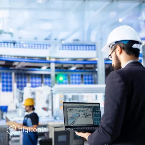 An engineer on a factory floor reading a plant layout on a laptop