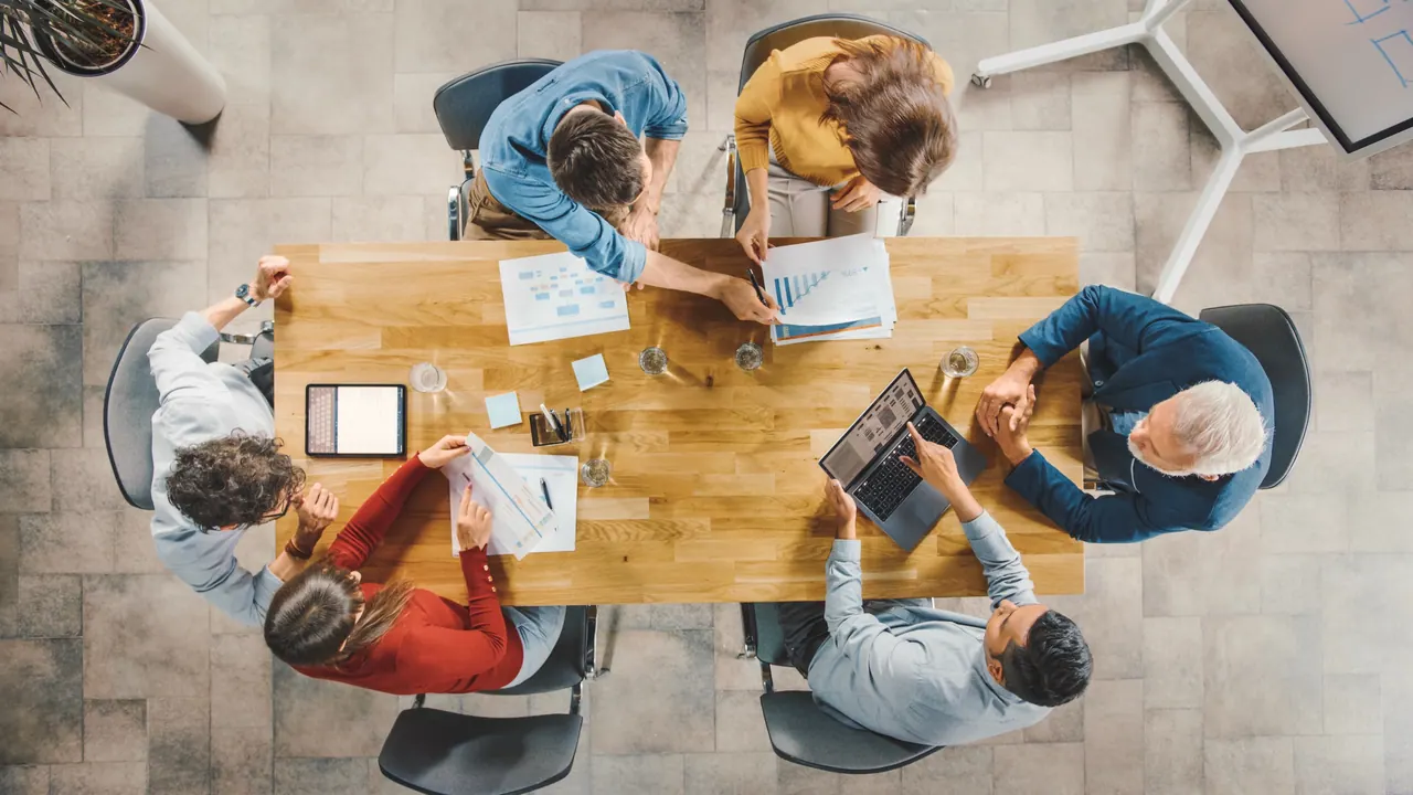 Forward deployed engineers and business colleagues around one table seen from above, working through architecture diagrams on laptops and paper.