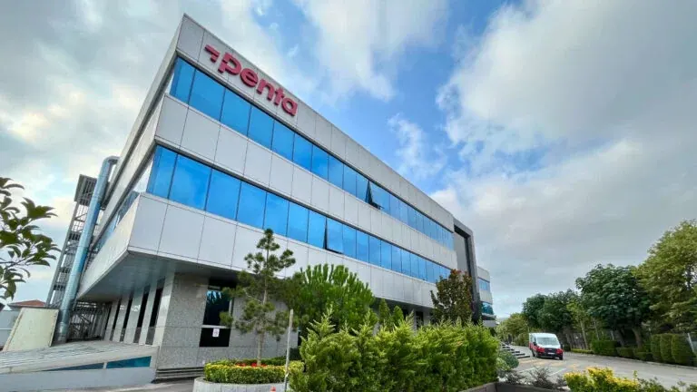 Penta Teknoloji’s headquarters: a three-storey glass and steel office block with the Penta wordmark along its top floor, under a clouded sky.