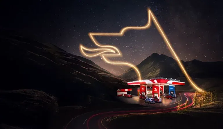 A Petrol Ofisi station lit up in a mountain valley at night, the brand’s mark drawn above it in a single ribbon of light following the road.