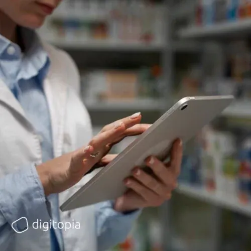 A pharmacist in a white coat working on a tablet in front of stocked shelves