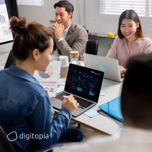 Four colleagues around a meeting table reading sales dashboards on a laptop
