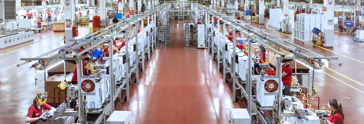 Two long washing-machine assembly lines running away from the camera inside a Vestel plant, operators in red shirts working at stations along both sides.