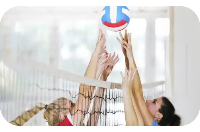 Two volleyball players reaching for the same ball above the net.