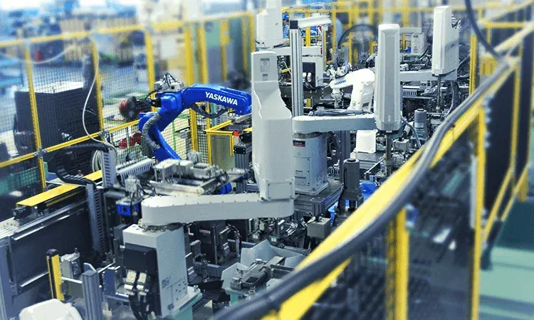 Robot arms and handling machinery on a production line behind yellow safety railings.